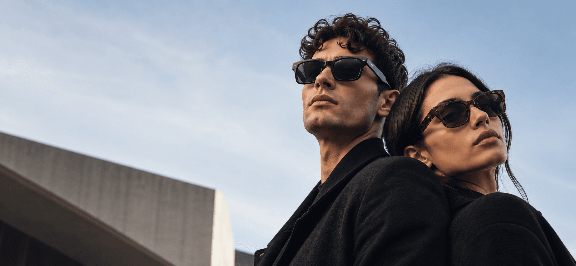 A man and a woman wearing sunglasses, photographed against a blue sky.