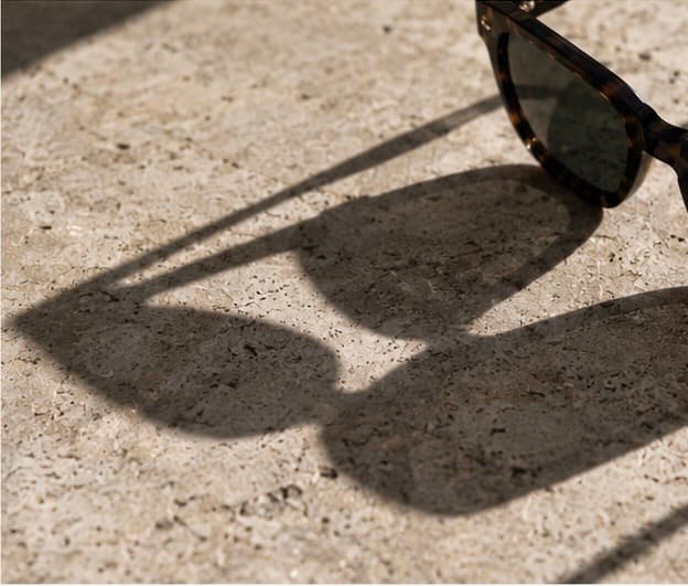 Tortoiseshell sunglasses resting on stone, casting a long shadow.